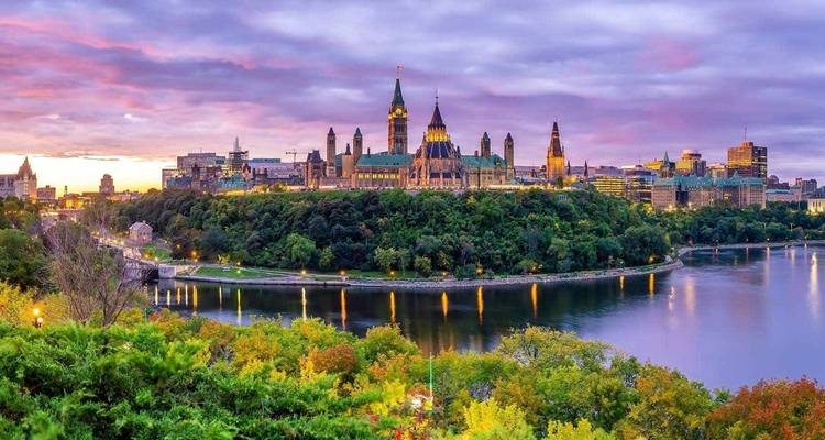 Scenic view of a city with iconic Gothic architecture along a river at sunset.