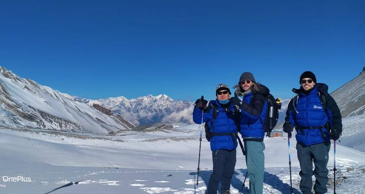 Drei Personen in blauen Jacken mit schneebedeckten Bergen hinter ihnen.