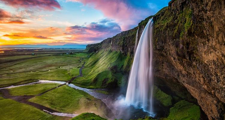 Hoge waterval die in een rivier stort met zonsondergangkleuren aan de hemel.