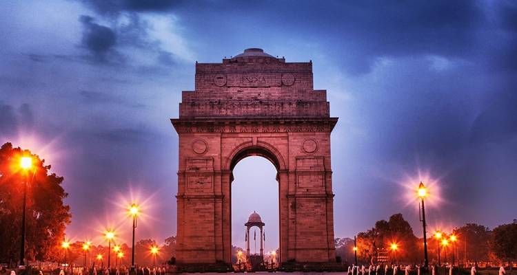 India Gate beleuchtet in der Dämmerung mit bewölktem Himmel.