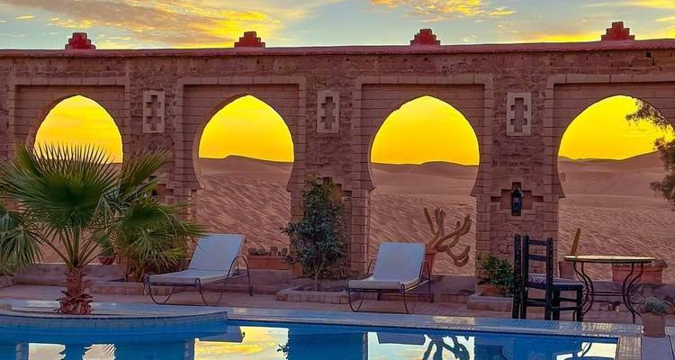 Poolside view with arches and sand dunes at sunset.