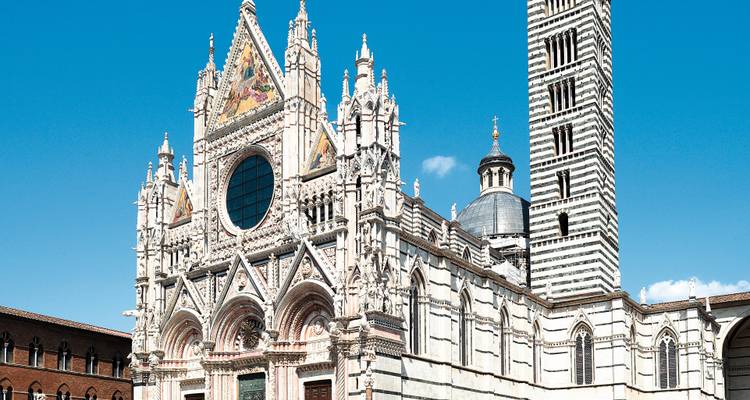 La façade gothique-romane élaborée de la Cathédrale de Sienne brille sous le soleil éclatant face à un ciel bleu pur.