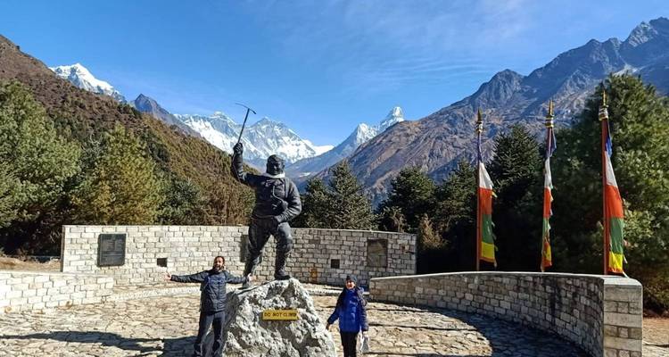 Zwei Personen neben einer Bergsteiger-Statue inmitten einer Berglandschaft.