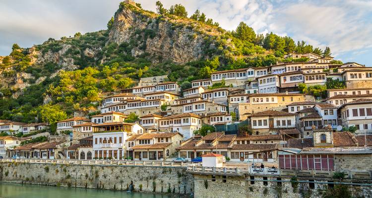 Vista panorámica de las casas otomanas blancas de Berat subiendo por una ladera verde sobre un paseo junto al río.