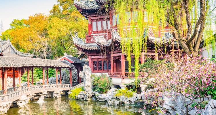 Rustige traditionele Chinese tuin met een vijver en bloeiende bomen.