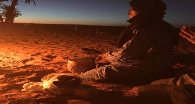 Una persona sentada junto a una fogata en el desierto durante el atardecer.