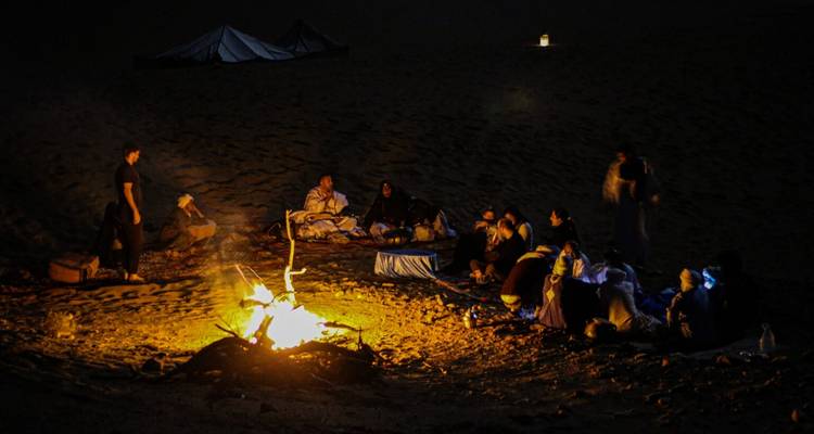 Un grupo de personas reunidas alrededor de una fogata en el desierto por la noche.