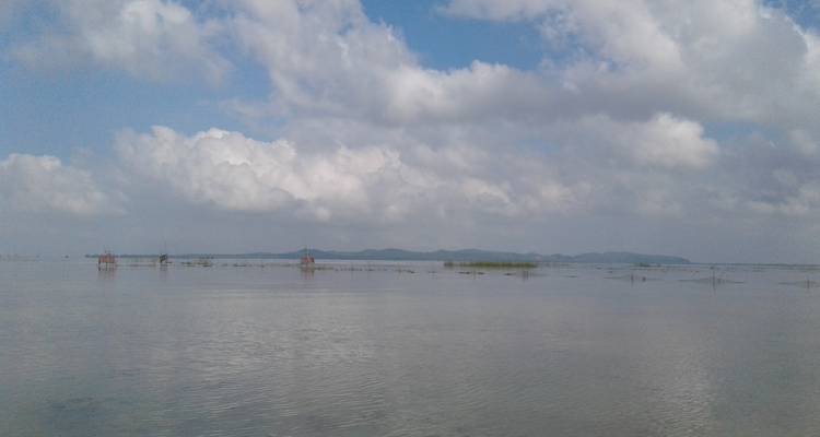 Uitgestrekt meer met bewolkte lucht en verre heuvels.