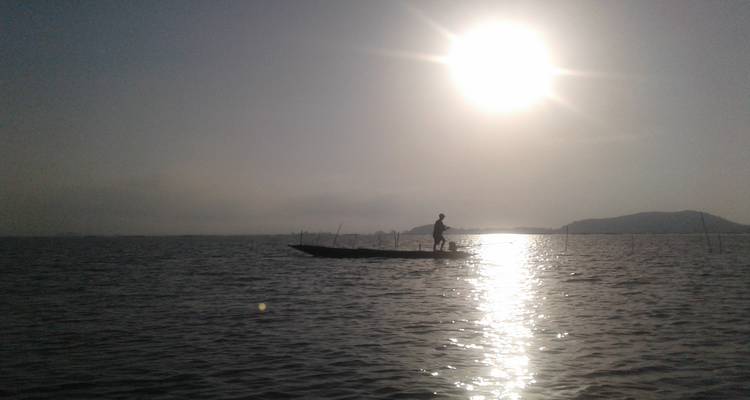 Silhouet van een visser tegen een heldere zon op een meer.