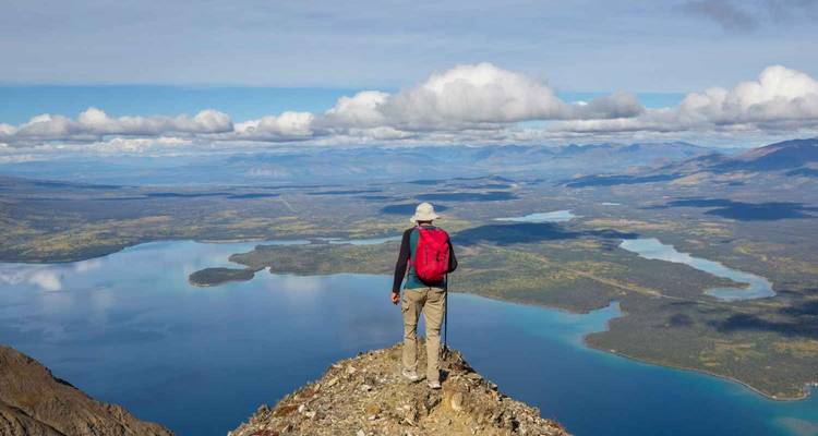 Persona de pie en la cima de una montaña contemplando un vasto lago y paisaje.