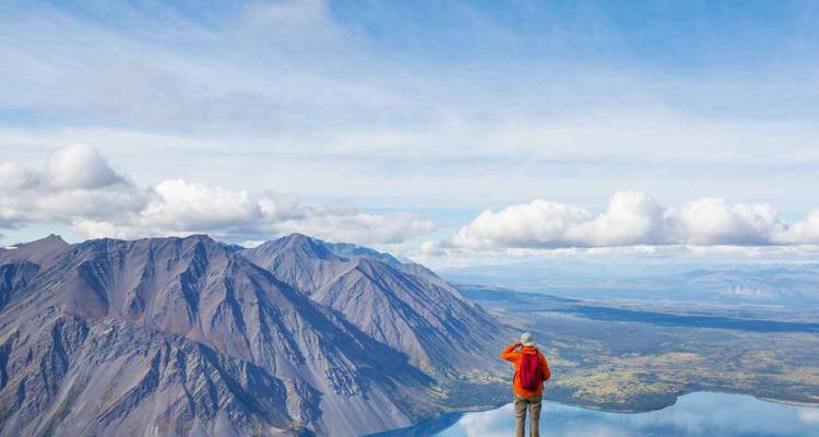 Persona de pie en un acantilado contemplando una cordillera y un valle.