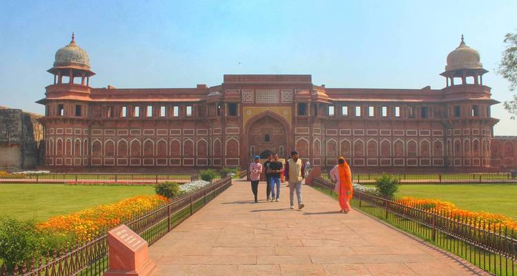 People walking towards a large red historic fort.
