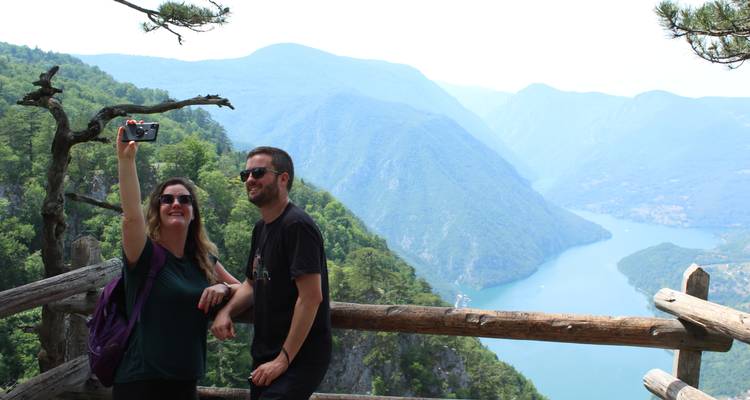 Pareja tomándose una selfie con vista panorámica de montañas y río.