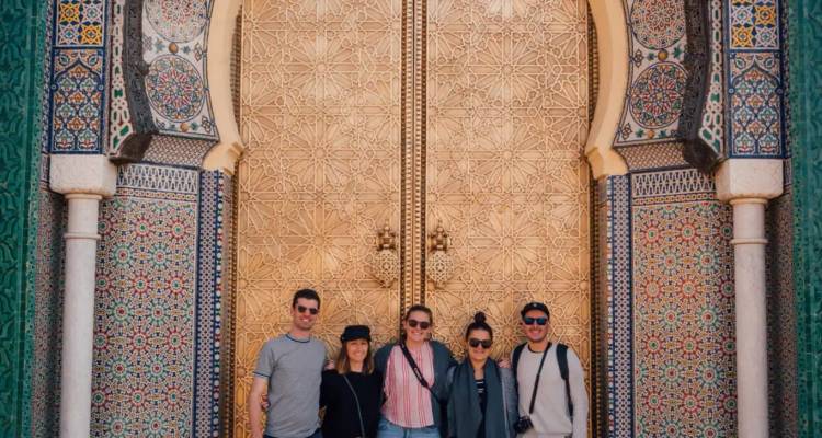 Amigos posando frente a las puertas doradas y ornamentadas del Palacio Real en Fez.