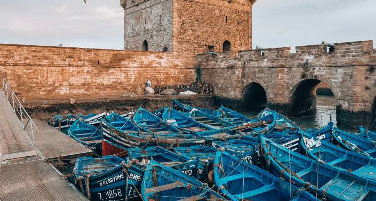 Flota de barcos de pesca de madera azul amarrados junto a los antiguos muros de la fortaleza en Essaouira.