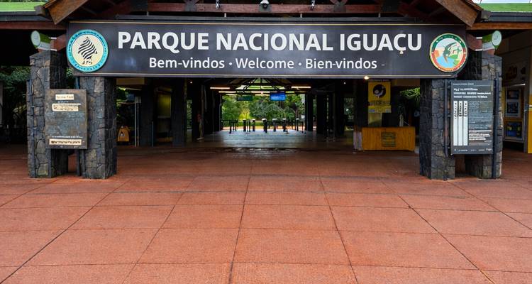 Pabellón de entrada del Parque Nacional Iguazú con letrero de bienvenida multilingüe y puertas abiertas hacia la selva tropical más allá.