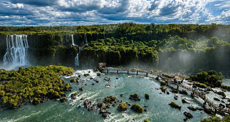 Otra vista panorámica de las Cataratas del Iguazú con spray elevándose desde múltiples cascadas y un sendero extendiéndose hacia el río.