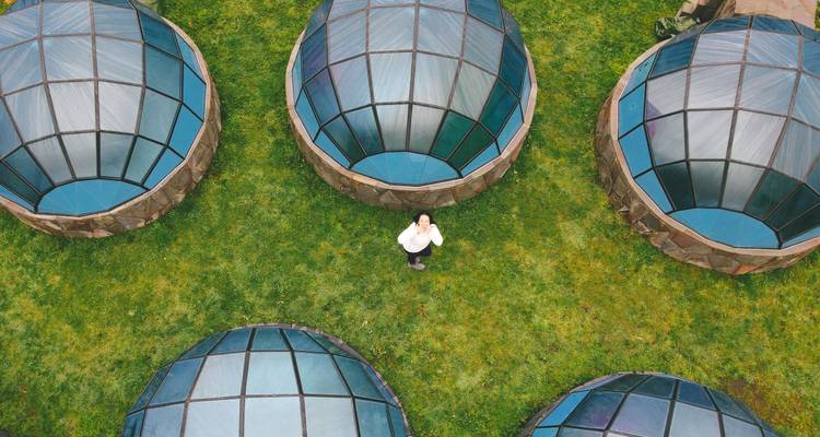 Vue de drone d'une personne devant plusieurs dômes transparents dans un champ.