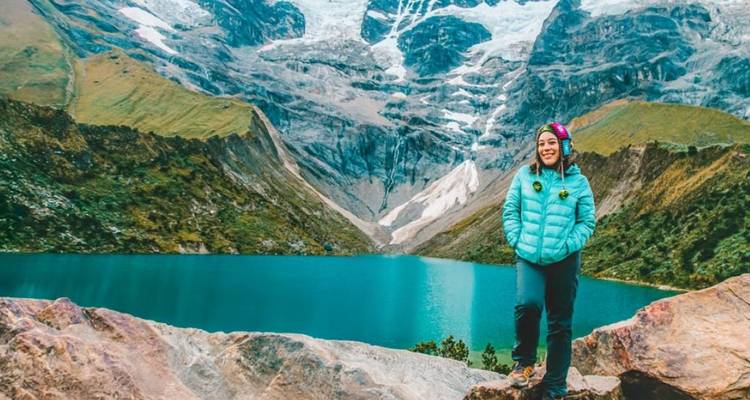 Viajero junto a un lago turquesa con montañas nevadas al fondo.