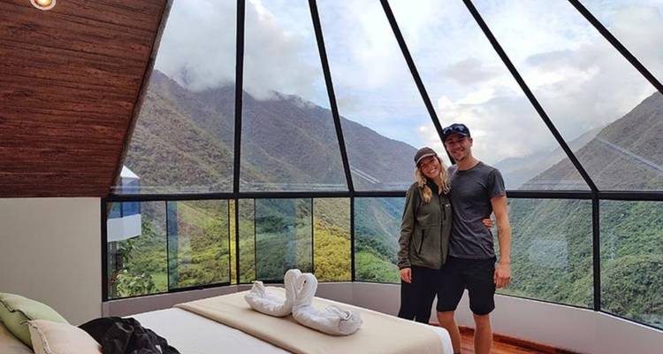 Pareja en dormitorio con paredes de cristal con vistas a las montañas.