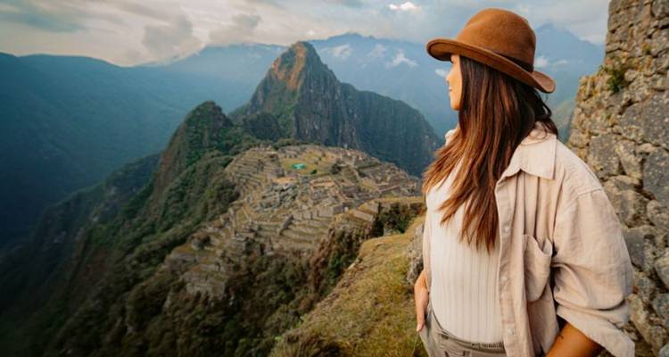Persona contemplando Machu Picchu con nubes dramáticas y montañas.