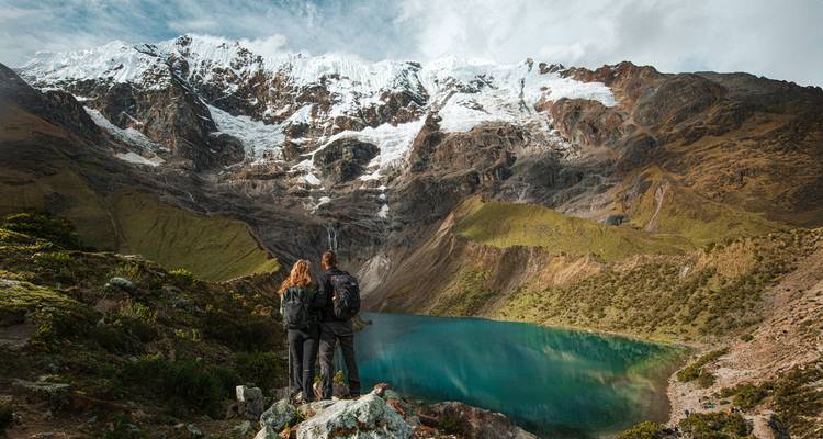 Pareja de pie ante un lago glacial turquesa rodeado de picos nevados.