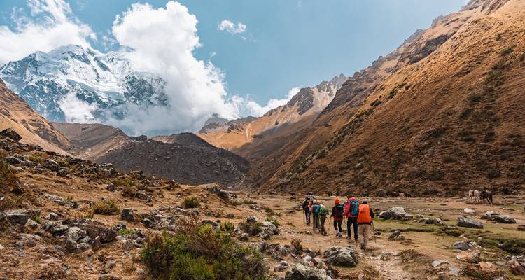 Grupo de senderismo caminando por un paisaje montañoso con una cumbre nevada.