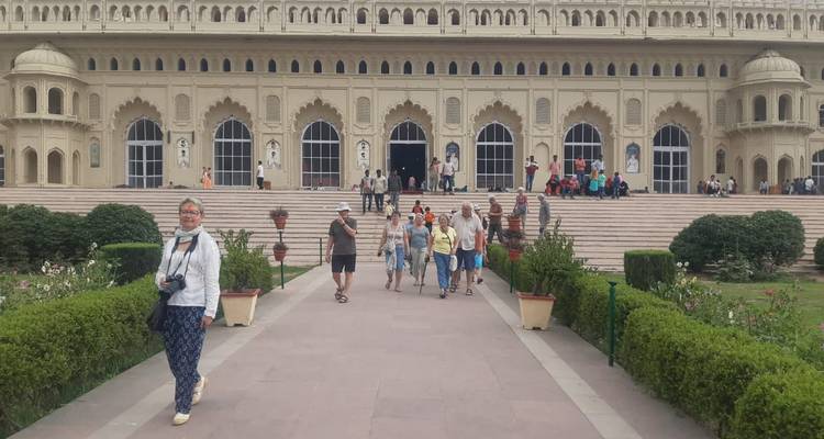 Des touristes marchant vers un grand bâtiment palatial avec des fenêtres cintrées et des détails architecturaux.