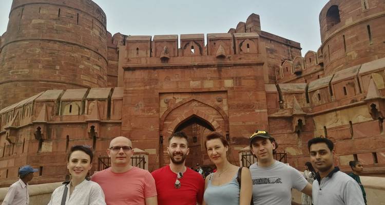 Groupe de personnes posant devant une grande fortification en grès rouge avec des sculptures complexes.