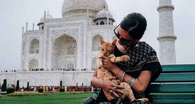 Woman holding a cat in front of the Taj Mahal.