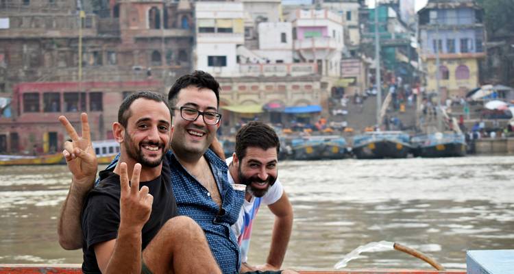 Trois amis profitant d'une promenade en bateau avec des ghats bondés en arrière-plan.