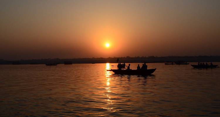 Silhouettes de bateaux sur une rivière au lever du soleil avec un soleil brillant.