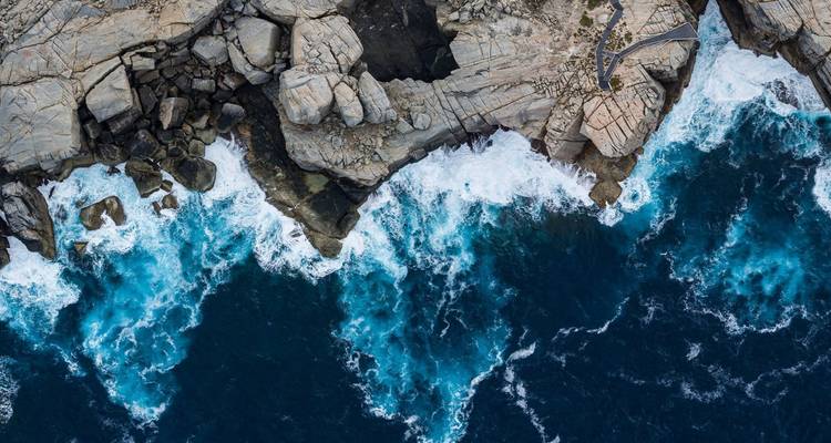 Luchtfoto van ruige granieten kliffen en diepblauwe golven die tegen de zuidelijke Australische kust slaan.