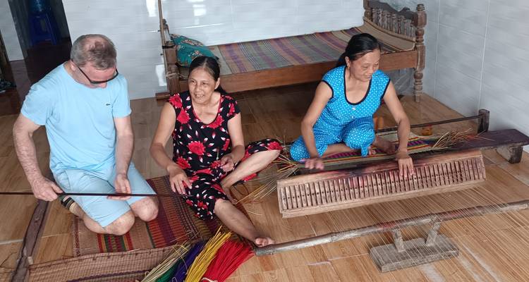 Two women and a man weaving indoors.