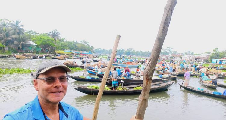 Ein lächelnder Reisender macht ein Selfie von einem kleinen Boot inmitten eines lebhaften Flussmarktes, der von vielen anderen Booten gefüllt ist.