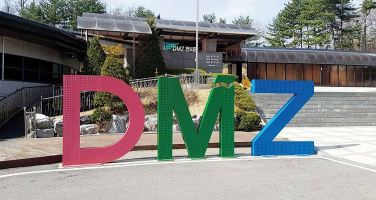 Kleurrijke drieletter DMZ-bord voor een bezoekerscentrum omgeven door sparren.