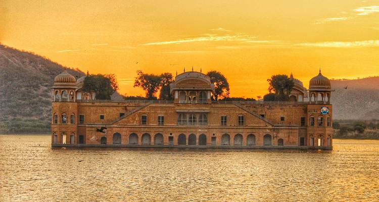 Jal Mahal illuminated at sunset, surrounded by water.