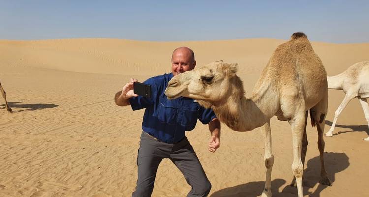Ein Mann, der ein Selfie mit einem Kamel in der Wüste macht.