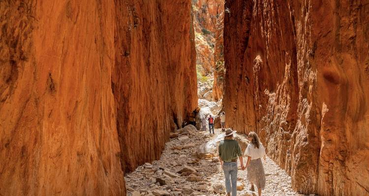 Wanderer gehen durch eine hoch aufragende rote Sandsteinschlucht mit sonnenbeschienenen Wänden im Outback