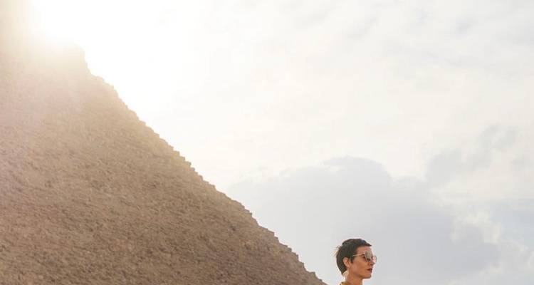 Personne à côté d'une pyramide avec un ciel lumineux derrière.