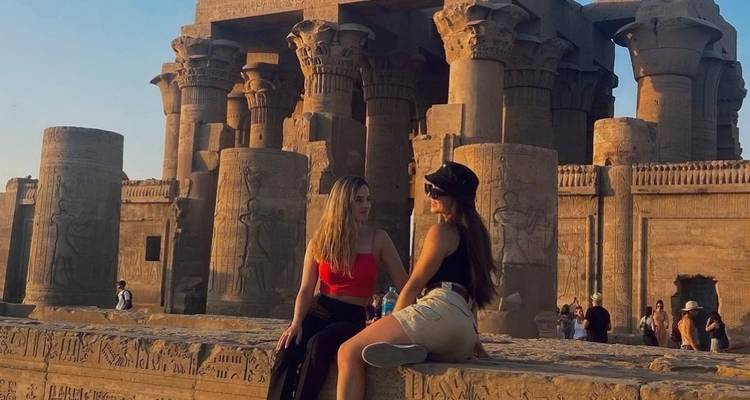 Zwei Frauen sitzen auf Ruinen mit einem ägyptischen Tempel im Hintergrund.