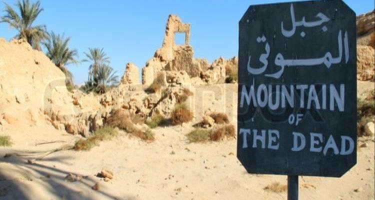 Panneau indiquant « Montagne des Morts » sur un fond de ruines antiques.
