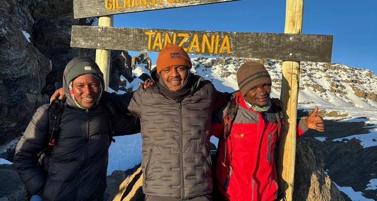 Trois hommes posant devant un panneau du Kilimandjaro.