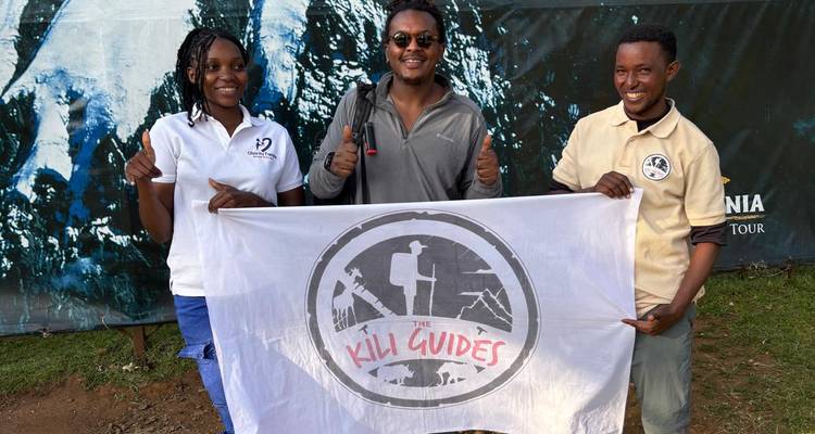 Trois personnes tenant une bannière Kili Guides, à l'extérieur.
