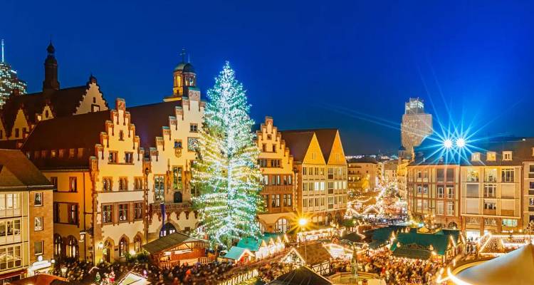 Mercado navideño europeo festivo por la noche con edificios de entramado de madera y luces brillantes en los árboles.