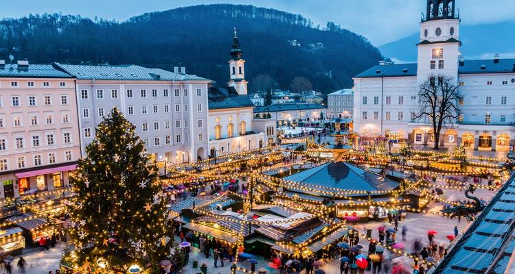 Festlicher Marktplatz in Salzburg mit bunten Ständen und einem großen Baum.