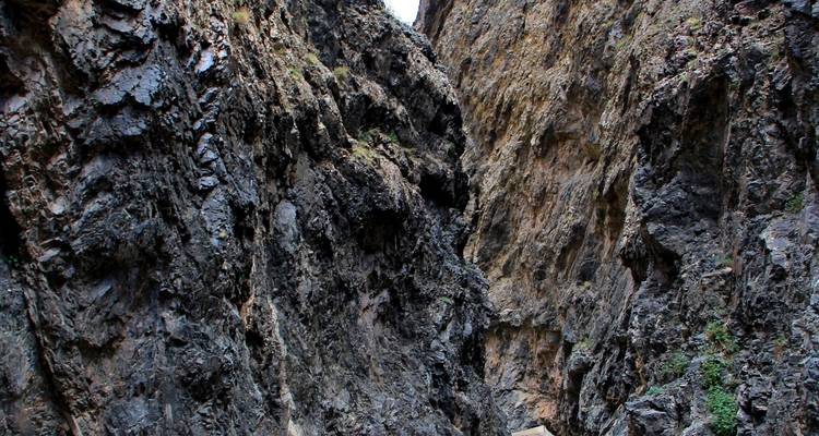 Smalle kloof met rotsige wanden en een heldere hemel zichtbaar erboven.