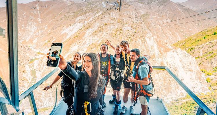 Avontuurlijke groepsselfie op een hoog platform met ruige bergen op de achtergrond.