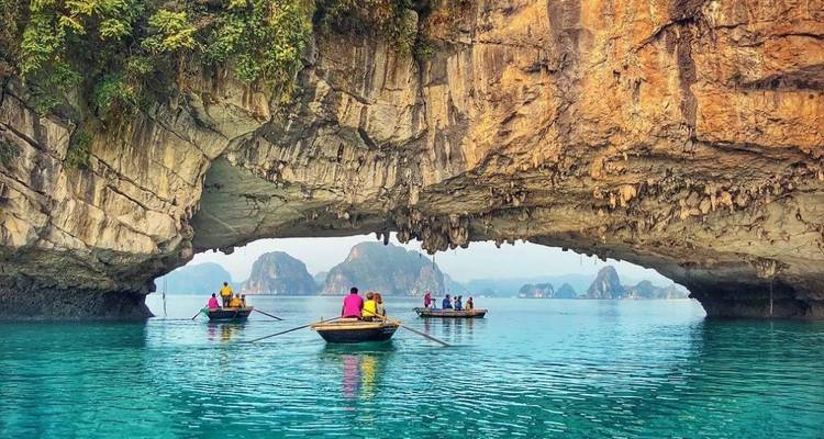 Boote mit rudernden Menschen unter einem Kalksteinbogen in der Halong-Bucht.