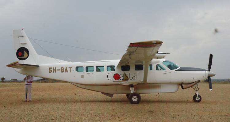 Petit avion stationné sur une piste en terre battue avec un ciel nuageux.
